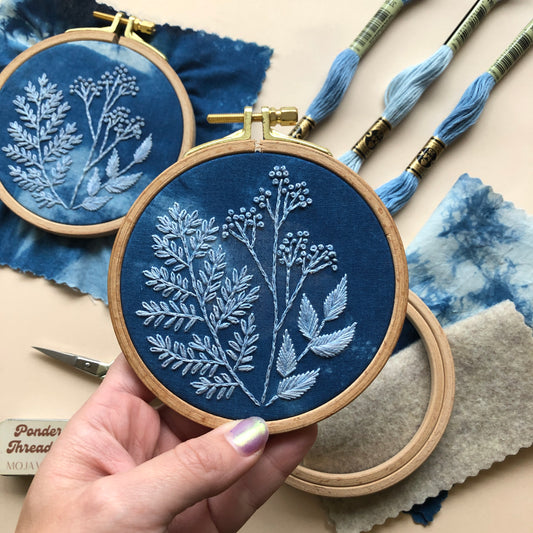 A completed cyanotype embroidery still in the hoop from the botanical DIY embroidery kit. Supplies and another finished embroidery