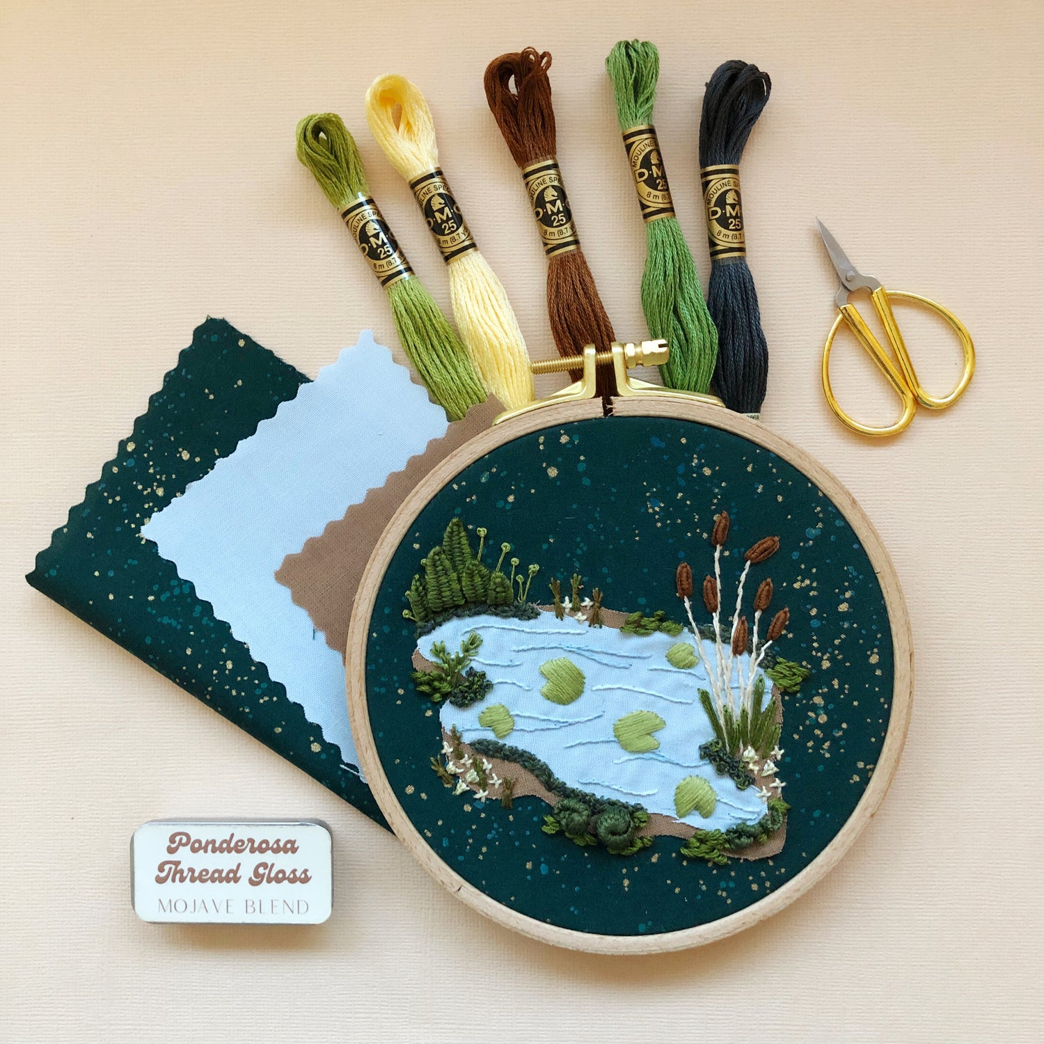 Contents of the 3D Lily Pad Pond advanced embroidery kit displayed: 5 skeins of thread, completed lily pad design still in the hoop, felt, fabric, and embroidery scissors (not included in kit).