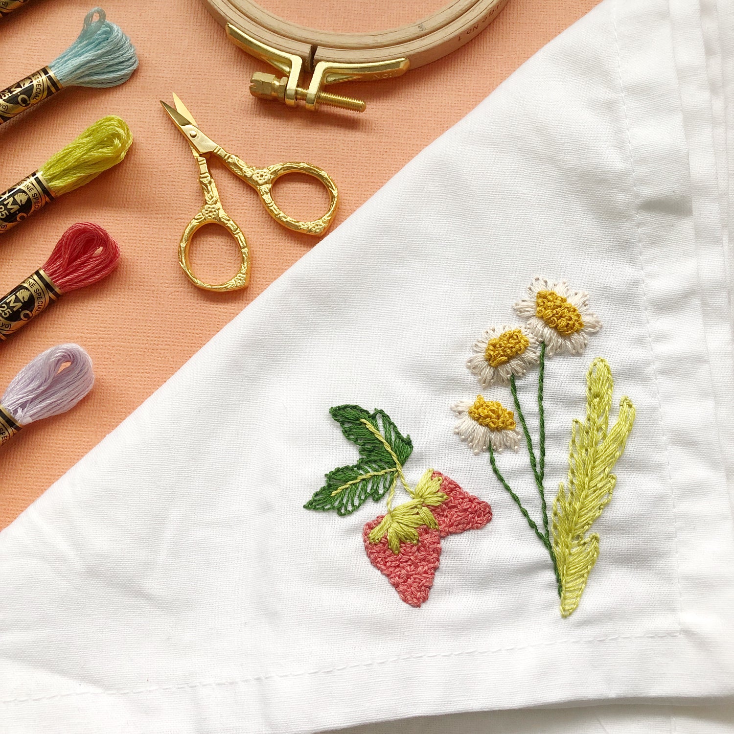 Example of 3 Forest Forage Stick and Stitch Embroidery Flowers Patterns Embroidered on White Napkin Surrounded by Other Embroidery Supplies