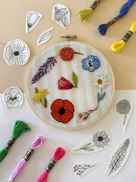 Completed embroidery design using wildflower stick and stitch embroidery pattern kit. Includes the 6 peel, stick, and stick designs around the completed project plus 6 skeins of thread (not included in kit)