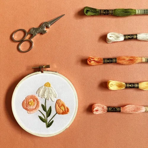 Some contents of the DIY Flower trio embroidery kit for beginners displayed: 5 skeins of thread, completed flower design still in the hoop and embroidery scissors (not included in kit)