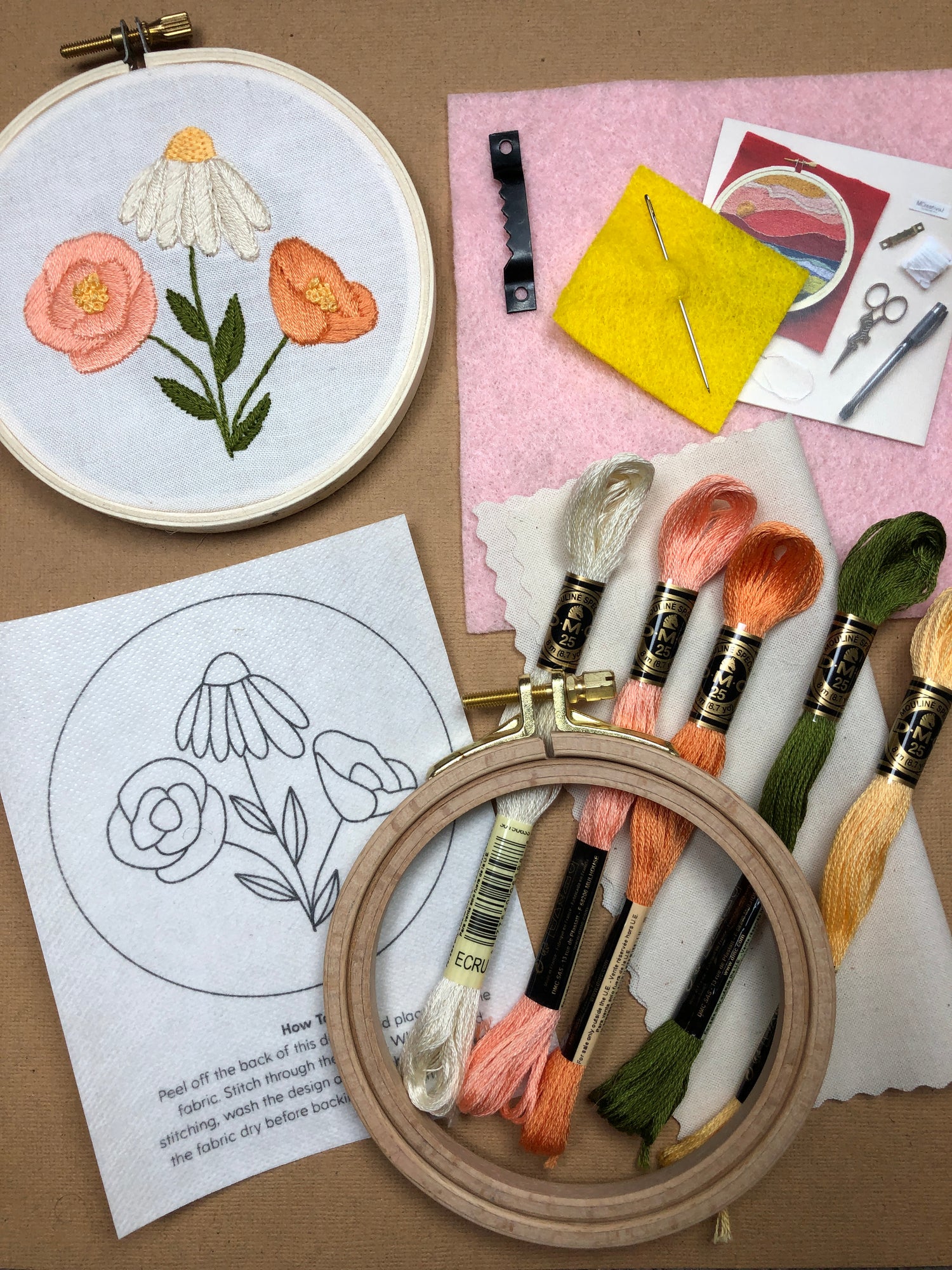 Contents of the DIY Flower trio embroidery kit for beginners displayed: 5 skeins of thread, completed flower design still in the hoop, transfer design, felt, sawtooth hanger hook, & instructions.