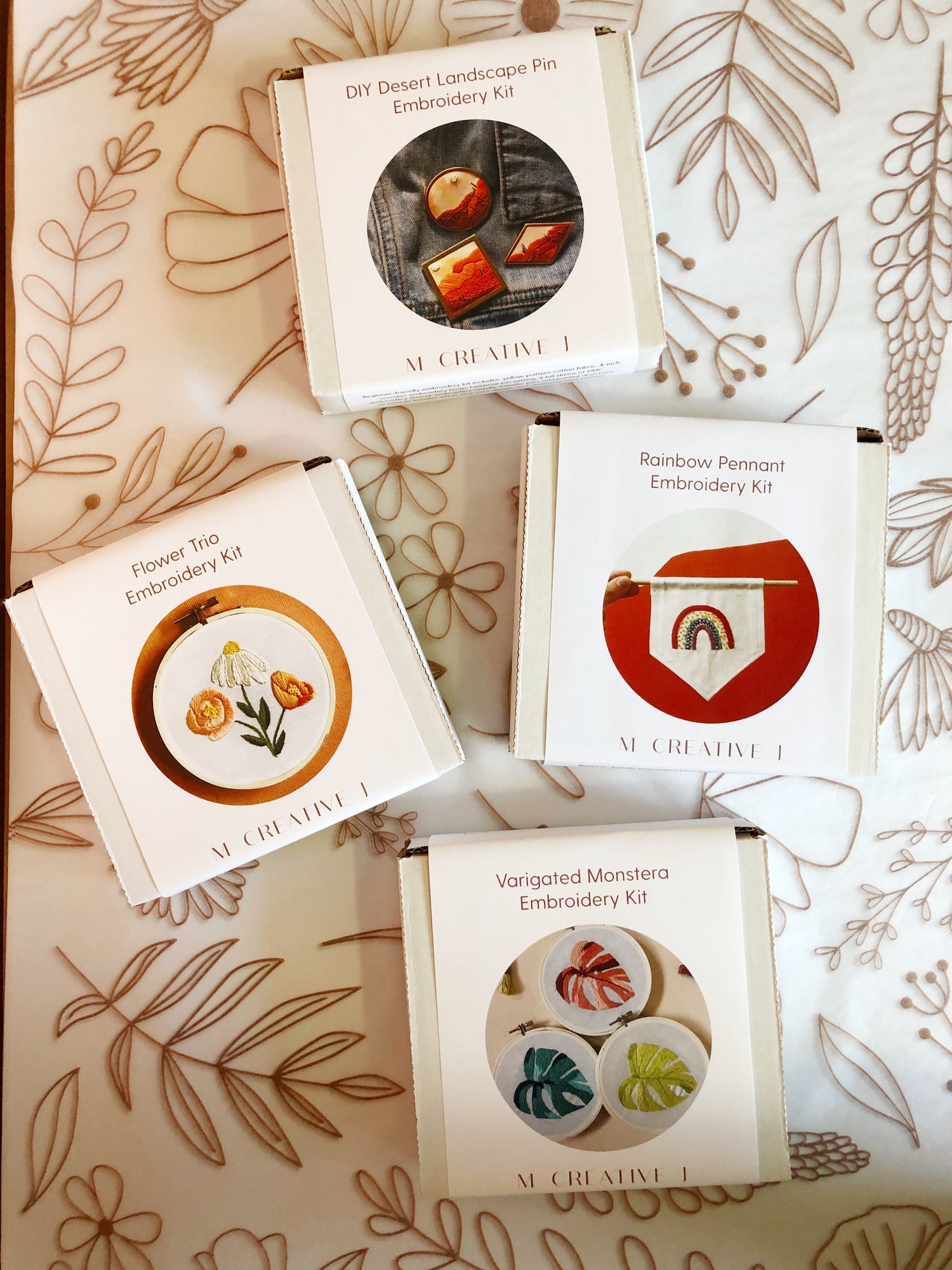 Boxes of kits for DIY Flower trio embroidery kit for beginners plus others like rainbow pennant, desert landscape pin, varigated monstera