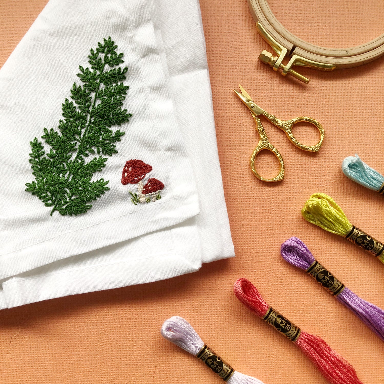 Example of Forest Forage Stick and Stitch Embroidery Patterns Embroidered on White Napkin Surrounded by Other Embroidery Supplies